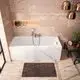Weiße Badewanne in modernem Design mit verchromter Armatur von Ideal Standard. An der Wand befinden sich beige Fliesen und eine kleine Ablage für Pflegeprodukte.